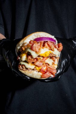 Güzel bir restoranda, üç etli, soğanlı, sarı ve beyaz peynirli ve pastırmalı lezzetli dev hamburger.