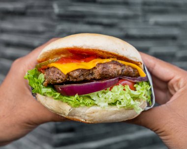 Elinde taze malzemeli klasik sığır burger tutan bir insan.