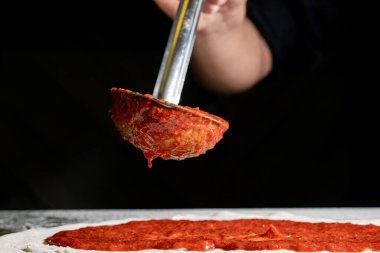 Restoranda pizza hazırlamak için domates sosu koyan biri.