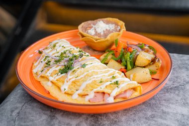 Delicious Mexican style homelete eggs with ham and cheese, accompanied by fried beans with cheese and potatoes with vegetables, perfect breakfast.
