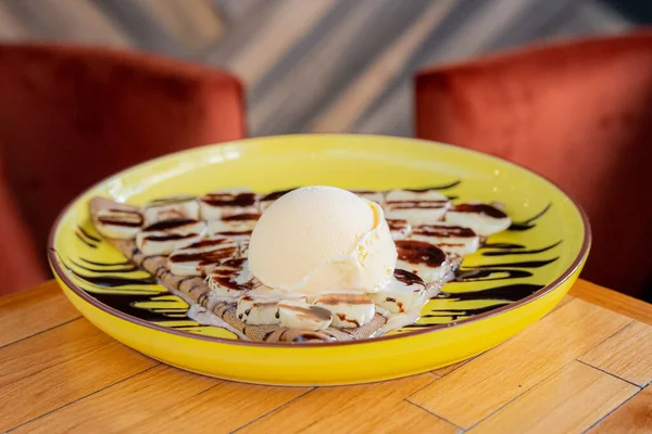 Delicious vanilla crepe with chocolate and a scoop of vanilla ice cream on top, on a nice yellow plate,