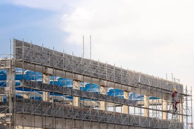 İnşaat alanında çalışan bir adam, yapı iskelesi ve gökyüzü arka planına sahip bir bina, inşaat faktörü için yapı iskelesi.