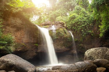 Ormandaki kayaların üzerinden süzülen ve yuvarlanan küçük şelale, parlak güneşli, Haew Suwat Waterfal