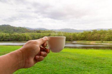 Sabahları elinde beyaz bir fincan sıcak espresso kahve fincanı ve doğa manzaralı güneş ışığıyla.