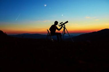 Astronomi teleskopu olan adam gece gökyüzüne, yıldızlara, gezegenlere, aya ve kayan yıldızlara bakıyor..