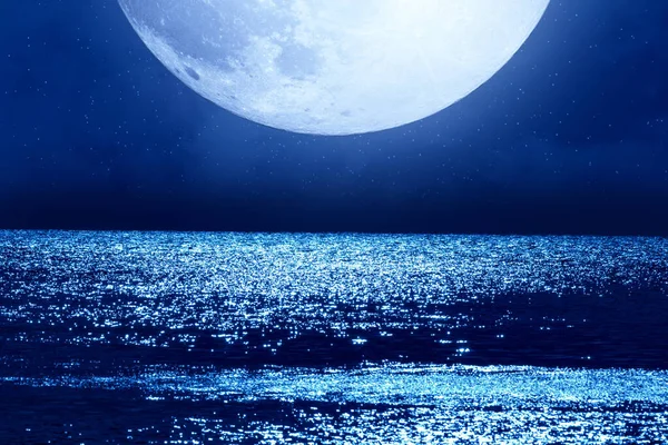 Full Moon with starry skies rising above ocean horizon.