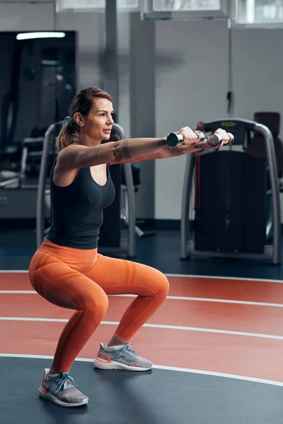 Sporty woman in gym exercising with light weight dumbbell.
