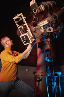 Astronomer with a big astronomical telescope in observatory doing science research of space and celestial objects.