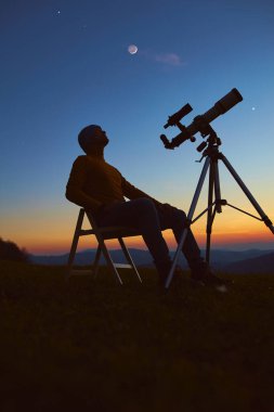 Man with astronomy telescope looking at the night sky, stars, planets, Moon and shooting stars.