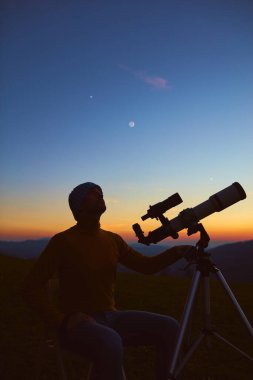 Man with astronomy telescope looking at the night sky, stars, planets, Moon and shooting stars.