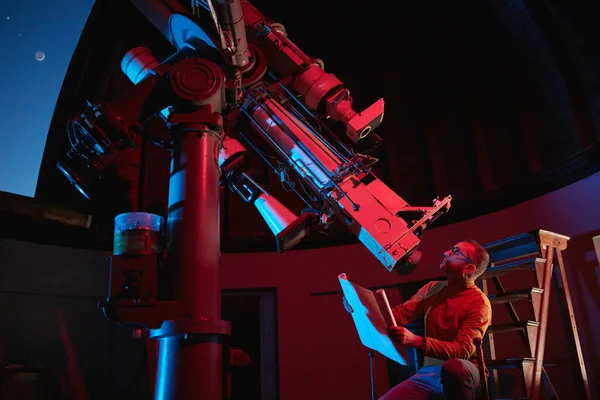 Astronomer with a big astronomical telescope in observatory doing science research of space and celestial objects.