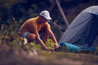 Man camping in nature, setting up the tent for overnight staying near forest river.