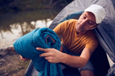 Man camping in nature, setting up the tent for overnight staying near forest river.