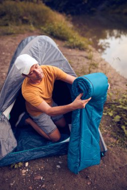 Man camping in nature, setting up the tent for overnight staying near forest river.