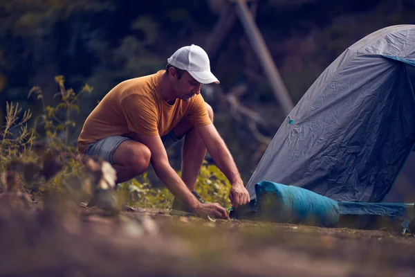 Man camping in nature, setting up the tent for overnight staying near forest river.