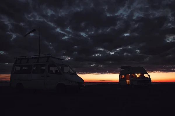 Camper van silhouette in nature near lake during sunset.