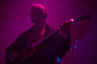 Sisli bir kulüpte renkli ışıklarla akustik gitar çalan müzisyen..