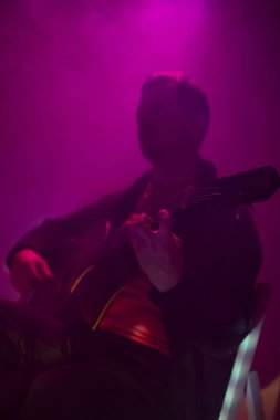 Sisli bir kulüpte renkli ışıklarla akustik gitar çalan müzisyen..
