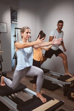 Genç bir kadın ve erkek spor salonunda pilates makinesinde kişisel antrenörleriyle egzersiz yapıyorlar..