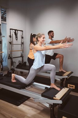 Genç bir kadın ve erkek spor salonunda pilates makinesinde kişisel antrenörleriyle egzersiz yapıyorlar..