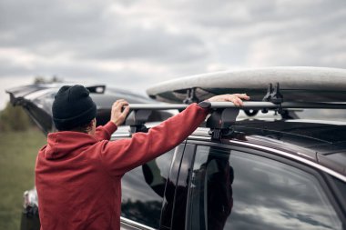 Rüzgâr sörfçüsü ve kampçı göl kıyısının yakınındaki bir arabadan araç gereçlerini boşaltıyor..