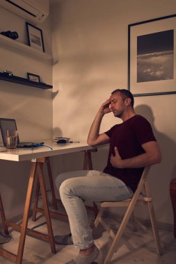 Evde dizüstü bilgisayarla çalışırken midesi ve başı ağrıyan bir adam..