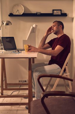 Evde dizüstü bilgisayarla uğraşırken başı ağrıyan ve bitkin hisseden bir adam..