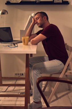 Evde dizüstü bilgisayarla çalışırken uyuyan ve başı ağrıyan bir adam..