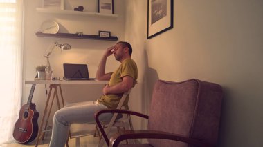 Evde dizüstü bilgisayarla uğraşırken başı ağrıyan ve bitkin hisseden bir adam..