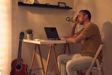 Evde dizüstü bilgisayarla uğraşırken başı ağrıyan ve bitkin hisseden bir adam..