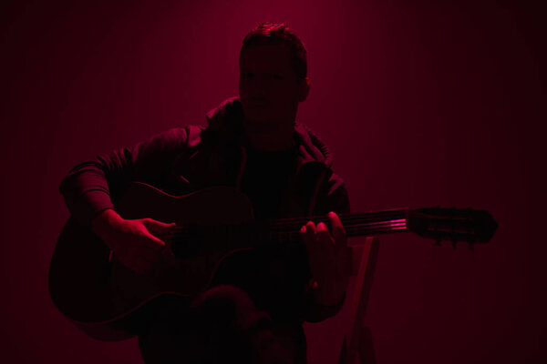 Musician playing acoustic guitar in a foggy club with colorful lights.