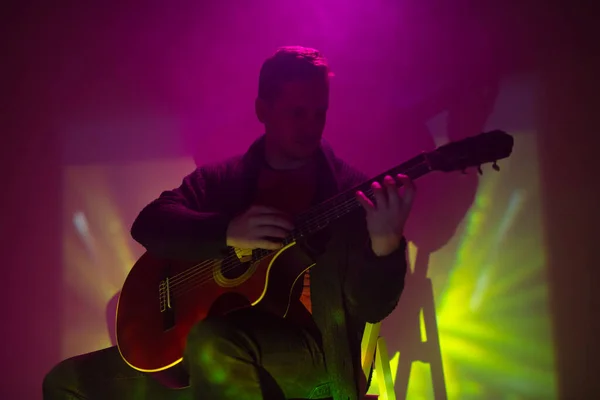 音楽家がカラフルなライトで霧のクラブでアコースティックギターを演奏 — ストック写真
