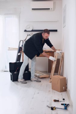 Yeni ahşap bir raf ve mobilya monte eden bir adam..