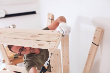 Yeni ahşap bir raf ve mobilya monte eden bir adam..