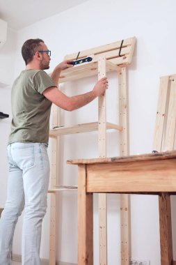 Yeni ahşap bir raf ve mobilya monte eden bir adam..