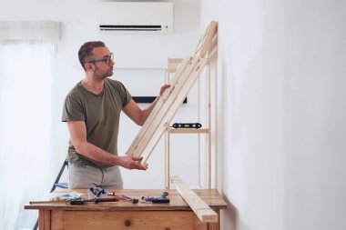 Yeni ahşap bir raf ve mobilya monte eden bir adam..