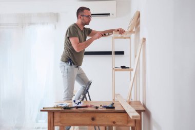 Yeni ahşap bir raf ve mobilya monte eden bir adam..