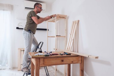 Yeni ahşap bir raf ve mobilya monte eden bir adam..