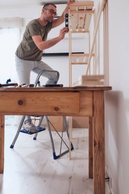 Yeni ahşap bir raf ve mobilya monte eden bir adam..