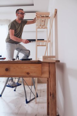 Yeni ahşap bir raf ve mobilya monte eden bir adam..
