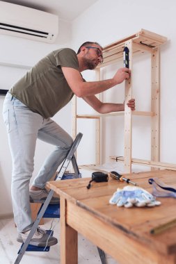 Yeni ahşap bir raf ve mobilya monte eden bir adam..