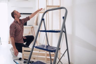 Yeni ahşap bir raf ve mobilya monte eden bir adam..