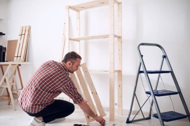 Yeni ahşap bir raf ve mobilya monte eden bir adam..