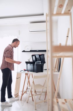 Yeni ahşap bir raf ve mobilya monte eden bir adam..