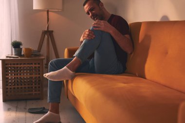 Evdeki koltukta oturan diz ağrısı olan bir adam..