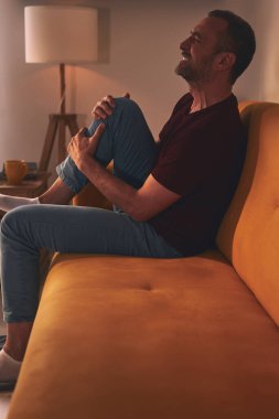 Evdeki koltukta oturan diz ağrısı olan bir adam..