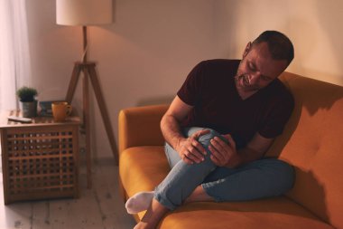 Evdeki koltukta oturan diz ağrısı olan bir adam..