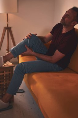Evdeki koltukta oturan diz ağrısı olan bir adam..