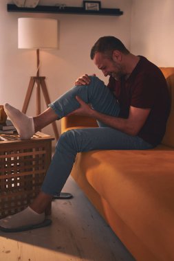 Evdeki koltukta oturan diz ağrısı olan bir adam..