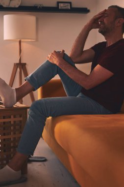 Evdeki koltukta oturan diz ağrısı olan bir adam..